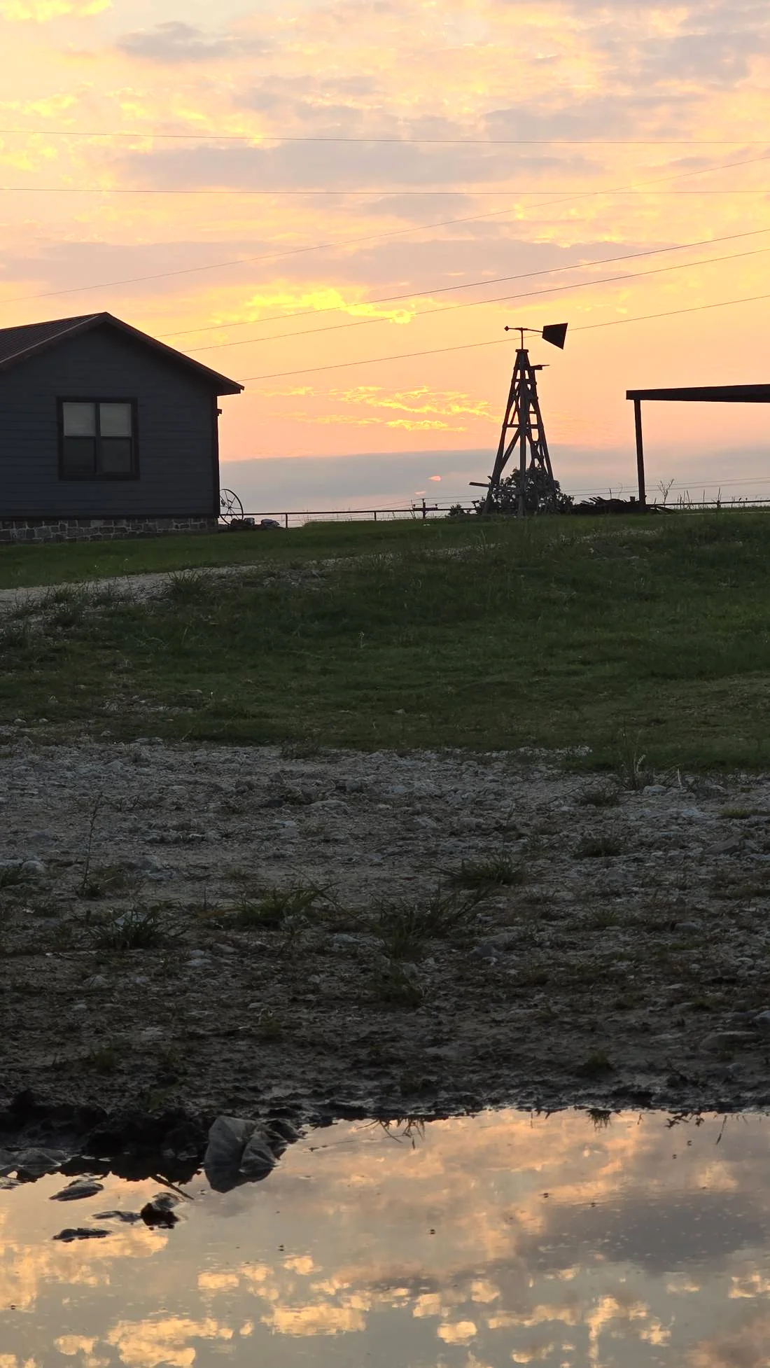 The bunkhouse and the windmill at Mosley Ranch at sunset, reflected in a puddle on the ranch road